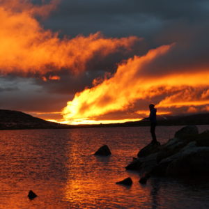 Fisker i silhuett med kraftig orange himmel og skyer i solnedgang